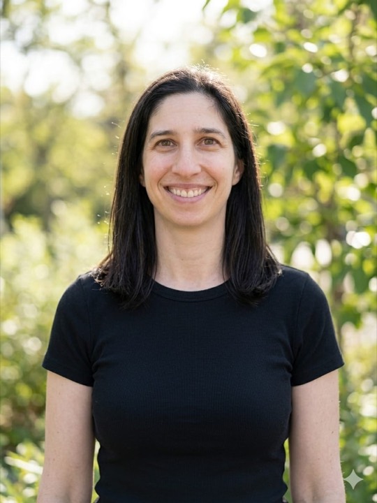 Ilana smiling outdoors in front of green trees